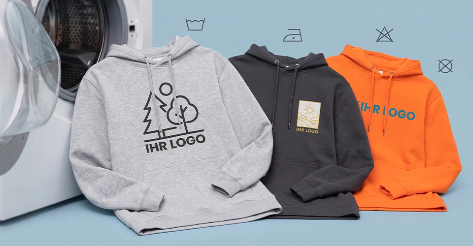 Individuell gestaltete Hoodies neben einer Waschmaschine auf blauem Hintergrund