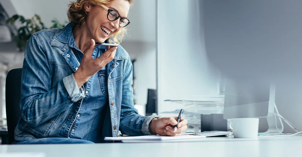 Kundin am Schreibtisch im Gespräch mit Kundenservice per Smartphone