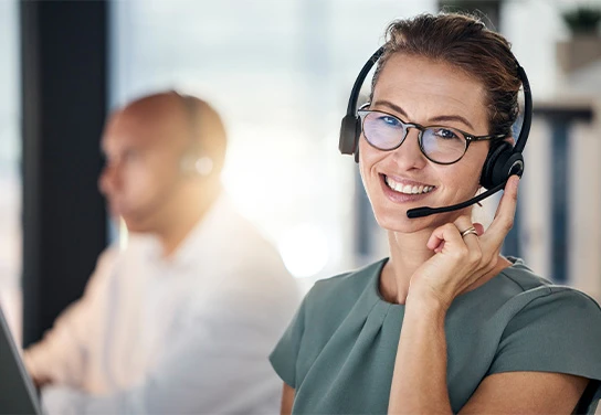 Mitarbeiterin im Kundenservice mit Headset blickt lächelnd in Kamera